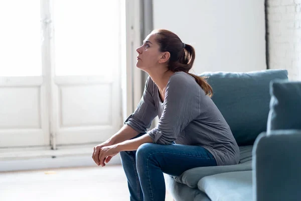 Mujer sentada sola en su sofá mirando hacia arriba mientras reflexiona como dejar de sentirse solo