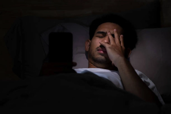 Persona despierta en la cama utilizando el teléfono celular en la oscuridad antes de dormir.